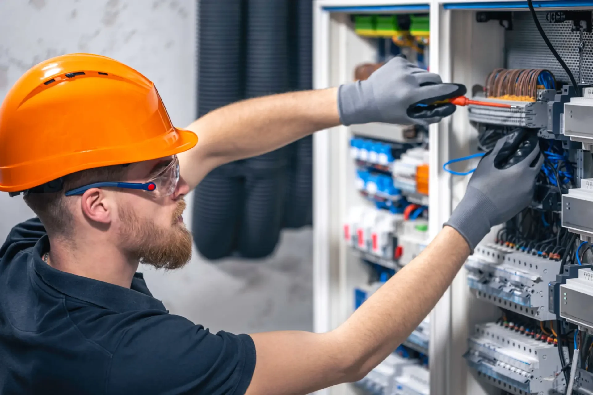 Electrician fixing wiring inside an electrical panel while wearing safety gear.