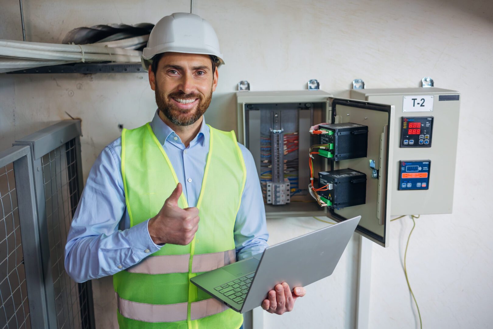 Engineer in safety gear giving thumbs up while working on electrical panel.