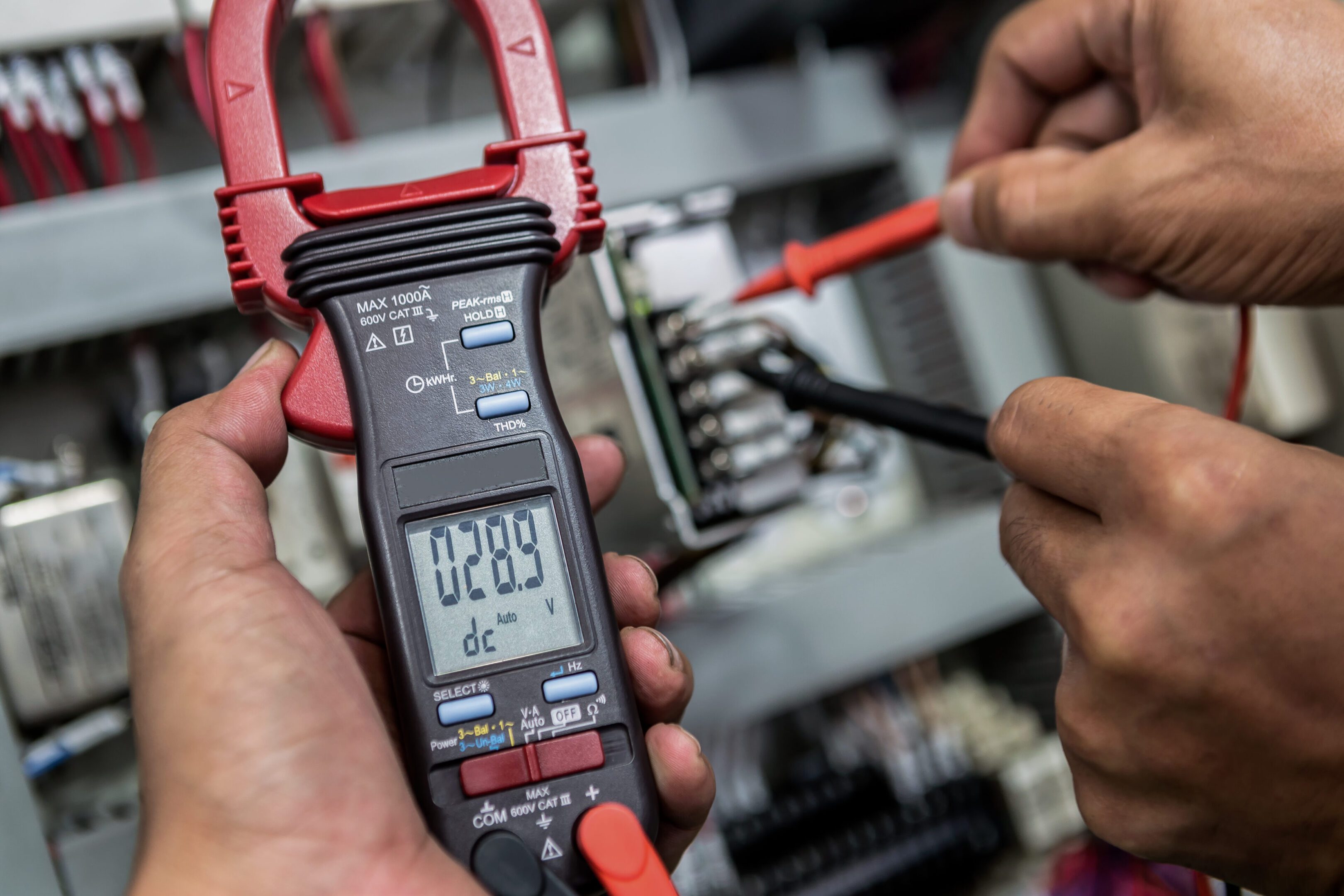 Technician using a clamp meter to measure electrical current in a circuit.