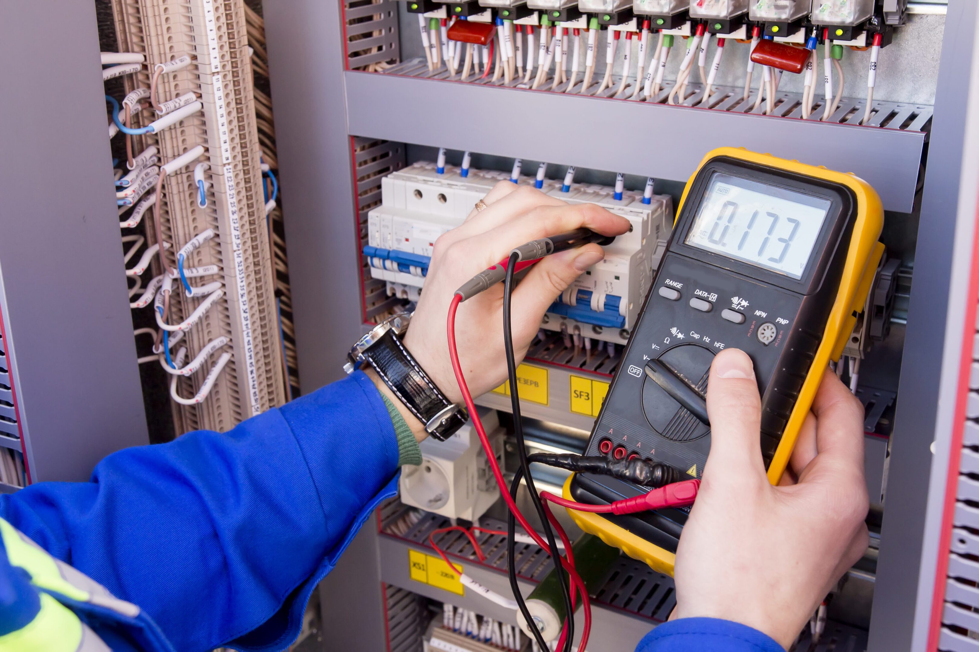 Technician measuring voltage in an electrical panel using a multimeter.